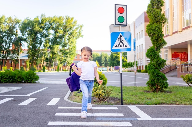 uma menina de escola atravessa a estrada em uma zebra perto do sinal de estrada pedestre atravessando indo para a escola com uma mochila o conceito de regras de trânsito
