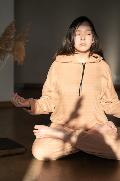 Uma menina de fato de treino bege senta-se no chão em posição de lótus e medita