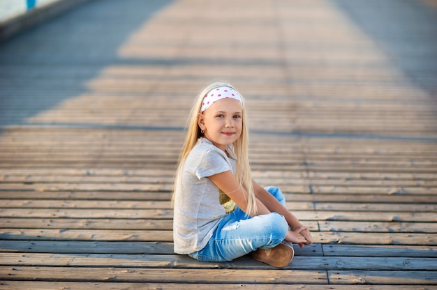 Uma menina de jeans e camiseta está sentada em um píer perto do Mar Báltico