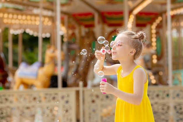Uma menina de óculos escuros soprando bolhas de sabão no parque no verão