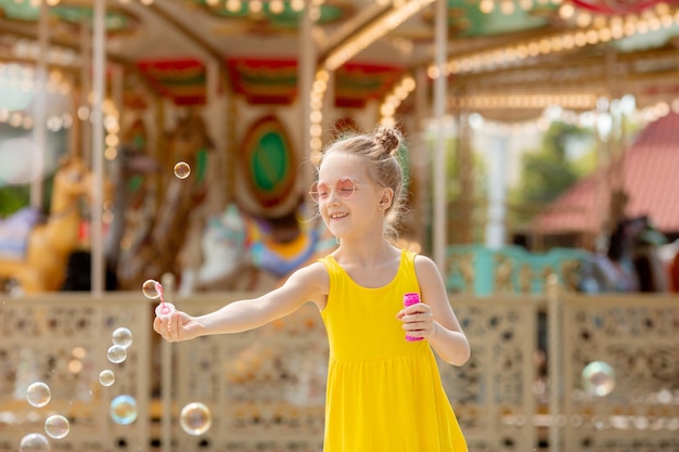 Uma menina de óculos escuros soprando bolhas de sabão no parque no verão