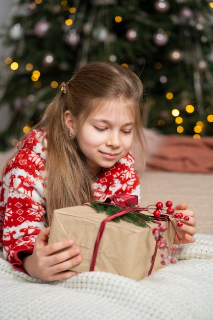 Uma menina de pijama de manhã cedo encontrou um presente do Papai Noel debaixo da árvore