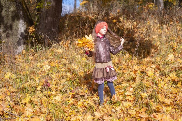 Uma menina de sete anos com cabelo comprido e uma jaqueta no parque no outono