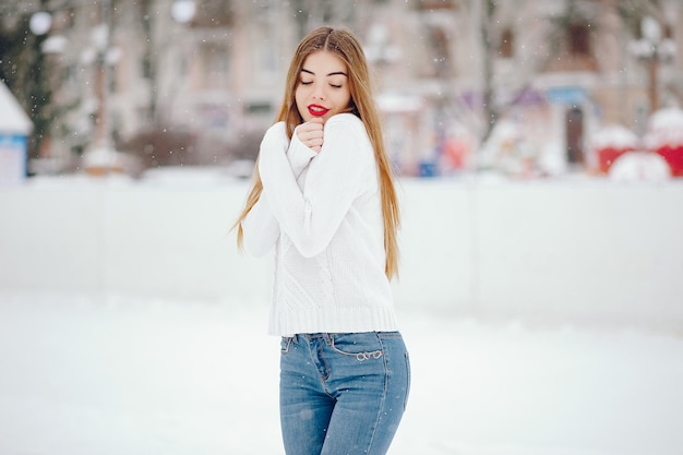 Uma menina de suéter branco de pé num parque de inverno