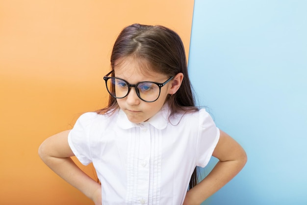 Uma menina de um ano com óculos com cara feia e mãos em seus lados