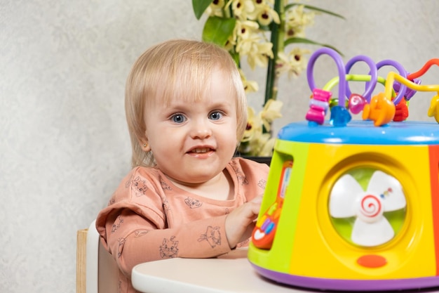 Uma menina de um ano e meio brinca com um brinquedo musical brilhante pressiona botões