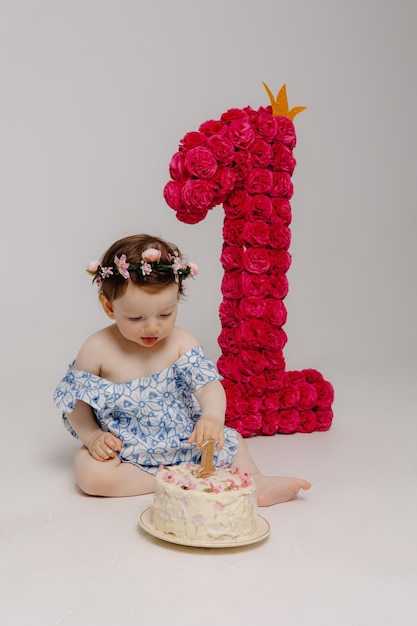 Foto uma menina de vestido azul está cortando um bolo com o número 1 nele