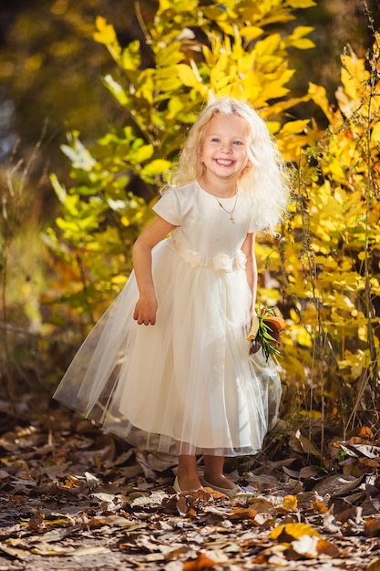 Uma menina de vestido branco que sorri em um fundo de folhas amarelas
