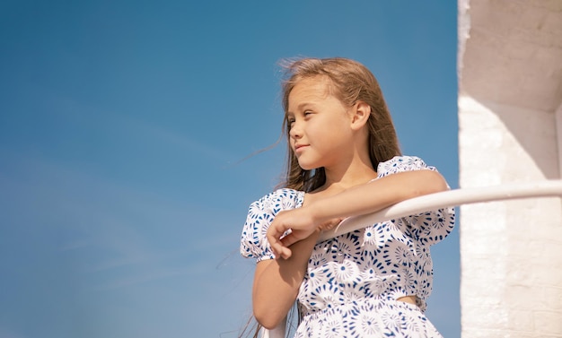 uma menina de vestido na praia com longos cabelos loiros no vento e olhando para o mar