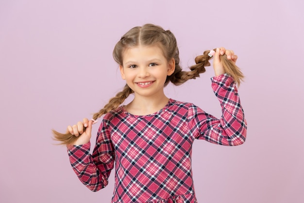 Uma menina de vestido segura as tranças com as mãos e sorri.