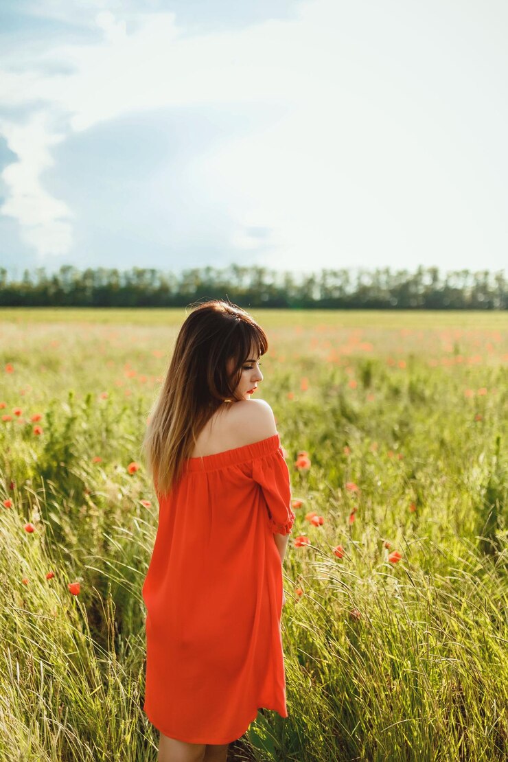 Foto uma menina de vestido vermelho acima do joelho está em um campo de papoulas durante o dia contra o céu