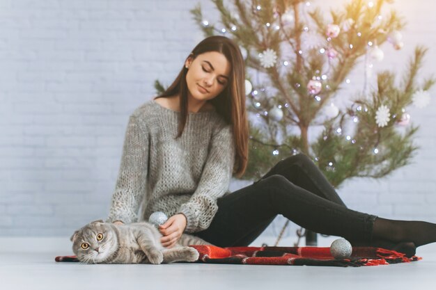 Uma menina decora uma árvore de Natal e brinca com seu gato.