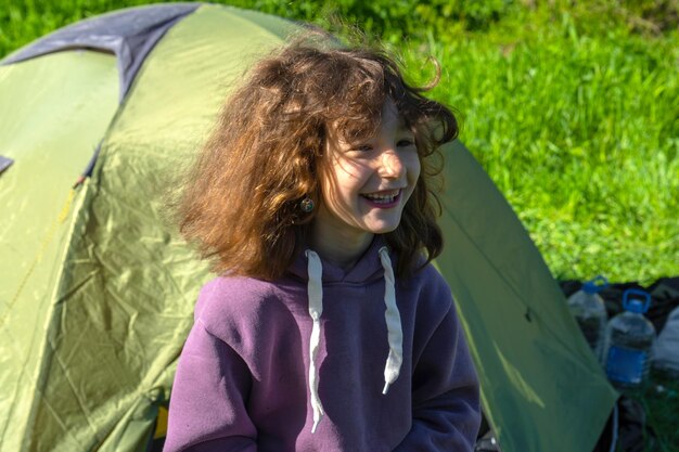 Uma menina desordenada ri contra o fundo de uma tenda de acampamento ao ar livre depois de dormir de manhã Recreação ao ar livre contra alergias Horário de verão