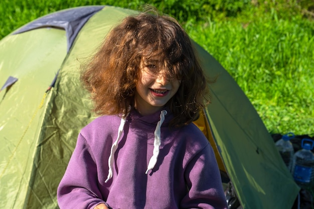 Uma menina desordenada ri contra o fundo de uma tenda de acampamento ao ar livre depois de dormir de manhã Recreação ao ar livre contra alergias Horário de verão