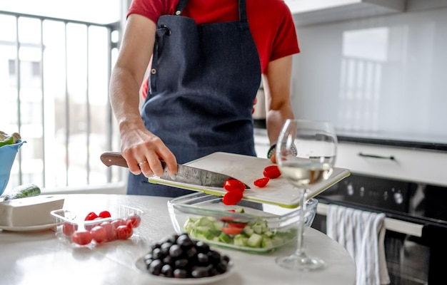 Uma menina despeja tomates cherry picados em uma tigela para a preparação de salada grega