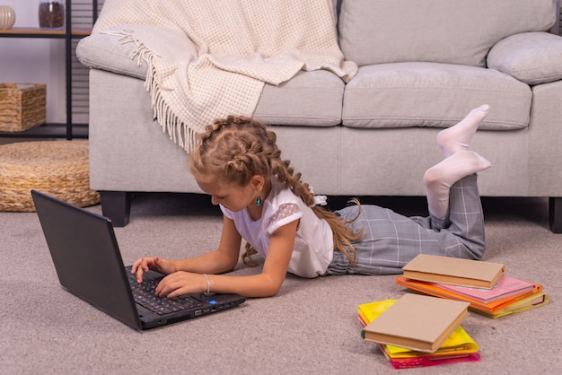 Uma menina do ensino fundamental está sentada em casa no sofá com um laptop em uma aula online