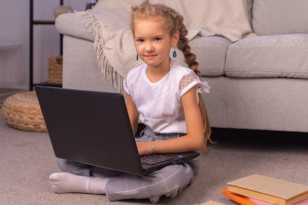 Uma menina do ensino fundamental está sentada em casa no sofá com um laptop em uma aula online