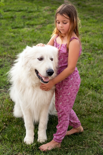 Uma menina doce e sorridente com seu amigo um cachorro maremma em um gramado verde