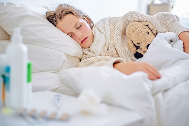 Foto uma menina doente com alta temperatura está dormindo na cama.