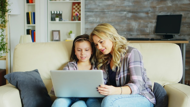 Uma menina e a mãe dela sentada no sofá da sala usando o laptop para fazer compras online.