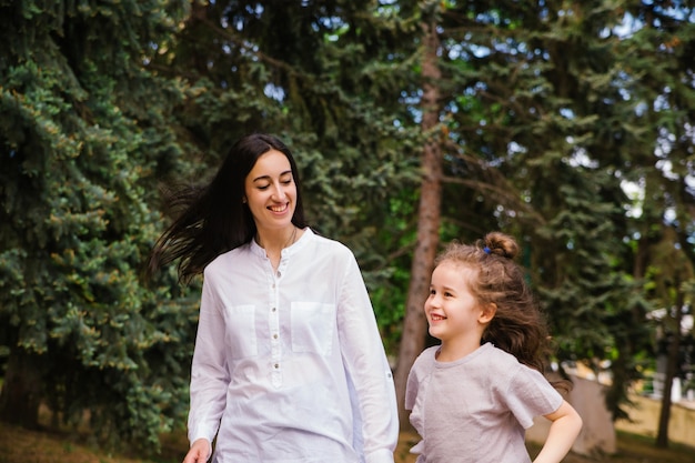 Uma menina e sua mãe correm pela calçada do parque. Jogo ativo na natureza.