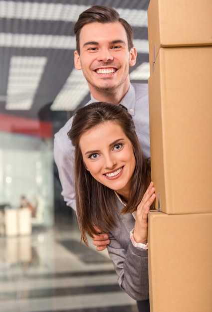 Foto uma menina e um homem espreitando por trás de uma caixa e sorrindo.