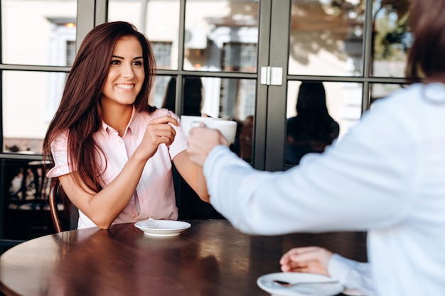 Uma menina e um jovem lade tilintando duas canecas de café em uma mesa de madeira em um café