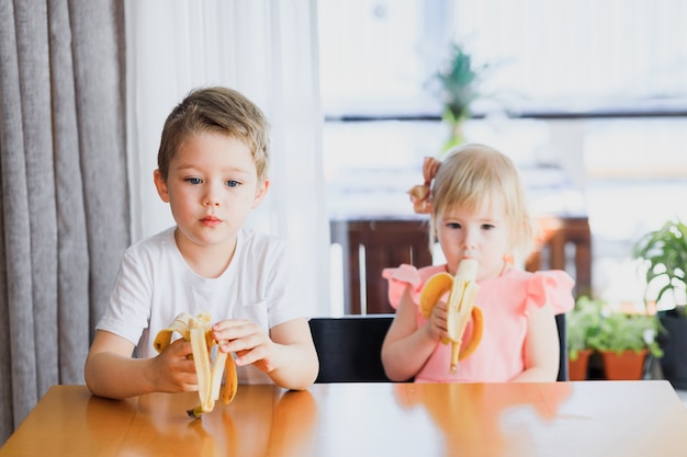 Uma menina e um menino comendo uma banana.