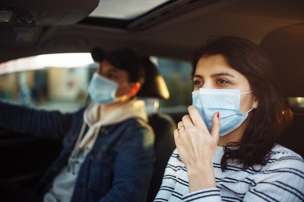 Uma menina e um menino dirigindo um carro durante a quarentena de coronavírus usando máscaras médicas