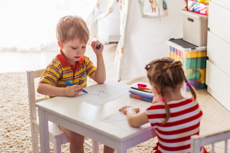 Uma menina e um menino em casa sentam-se à mesa e desenham com marcadores