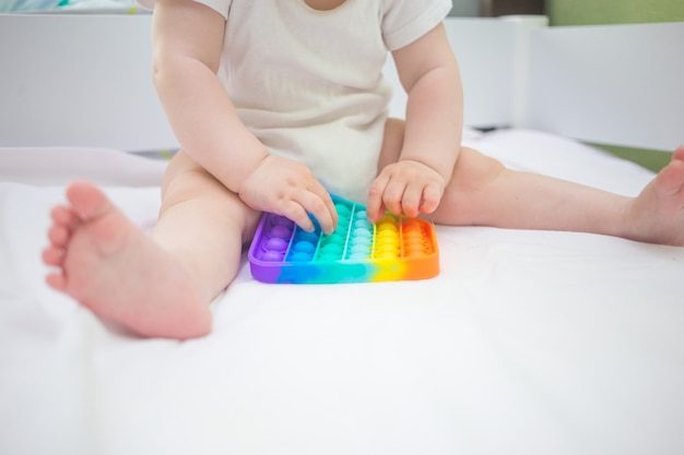 Foto uma menina em casa sentada na cama, jogando pop-it novo brinquedo anti-estresse, popular entre as crianças. idéia de desenvolvimento infantil.