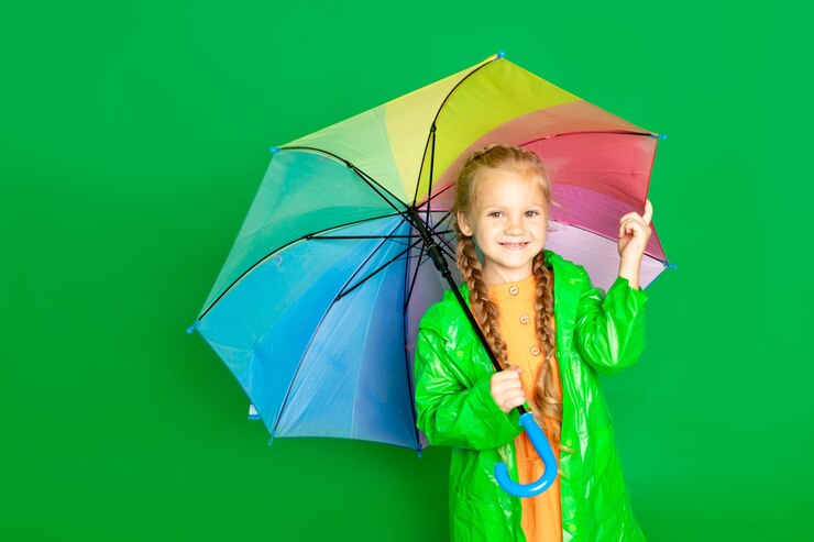 Foto uma menina em um fundo verde isolado com um guarda-chuva e um casaco de chuva sorri espaço para texto