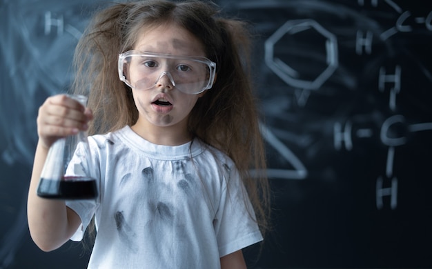 Uma menina em um laboratório escolar realiza experimentos em uma explosão de aula de química em um frasco