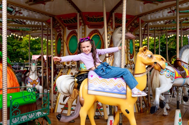 Uma menina em um parque de diversões anda em um carrossel e sorri de felicidade, o conceito de fim de semana e férias escolares