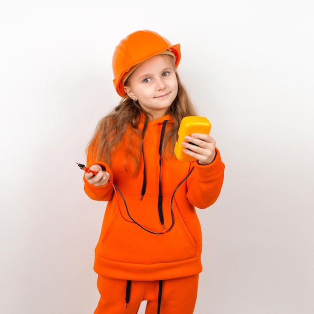 Uma menina em um terno laranja e um capacete de construção segurando um conceito de multímetro de um jovem eletricista retrato fundo branco dia do trabalho