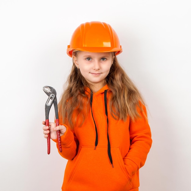 Uma menina em um terno laranja e um capacete de construção segurando uma chave inglesa um conceito de jovem trabalhador Retrato fundo branco Dia do Trabalho