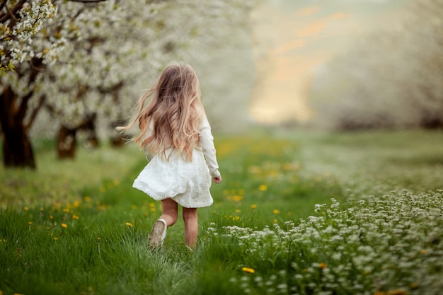 uma menina em um vestido branco e cabelo loiro é executado no jardim primavera florescendo