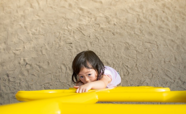 Uma menina em um vestido listrado sobe as escadas em um playground de areia. Tiro a partir do topo