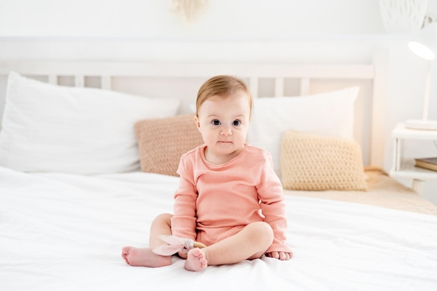 Uma menina em uma cama em um quarto brilhante em uma roupa rosa sorrindo ou rindo