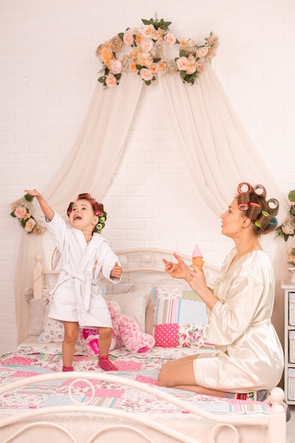 Uma menina encantadora com a mãe em rolos de cabelo brinca com bolas de sabão.