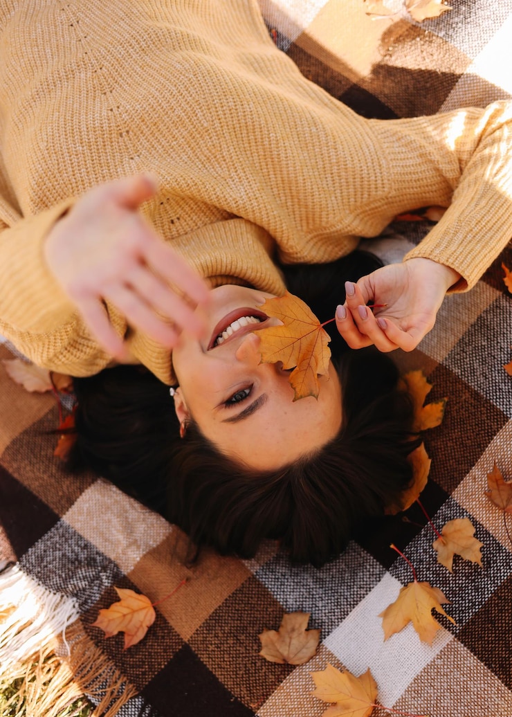 Foto uma menina engraçada e alegre pega folhas de outono sobre um cobertor no parque de outono.