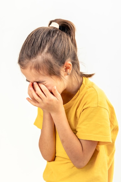 Uma menina está chorando cobrindo o rosto com as mãos em um fundo branco