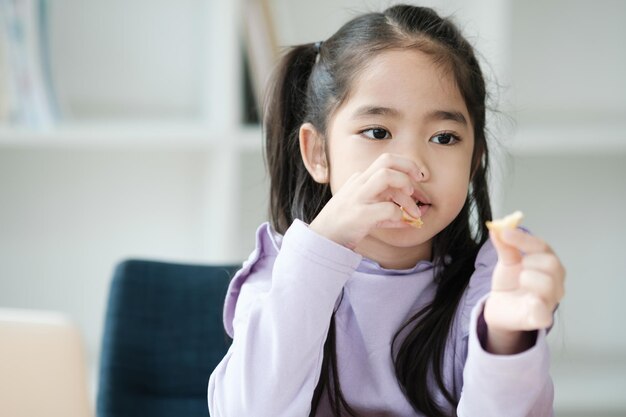 Uma menina está comendo um lanche enquanto está sentada em uma cadeira