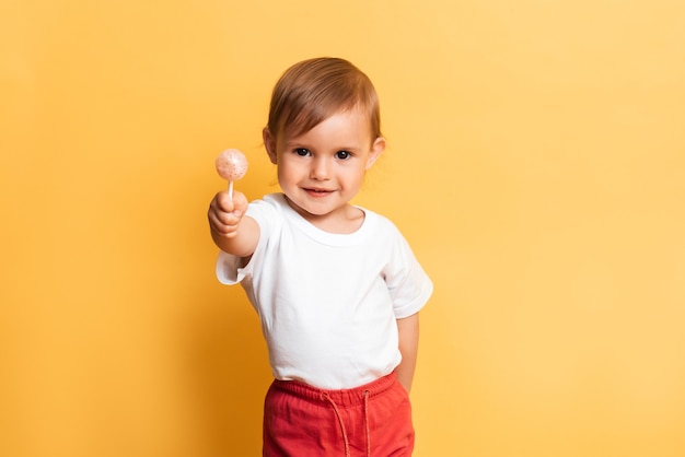 Uma menina está comendo um pirulito doce no palito. fundo amarelo. o conceito de prevenção da cárie e diabetes em crianças.