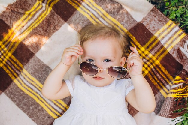 Uma menina está deitada em uma colcha xadrez e experimentando óculos de sol.