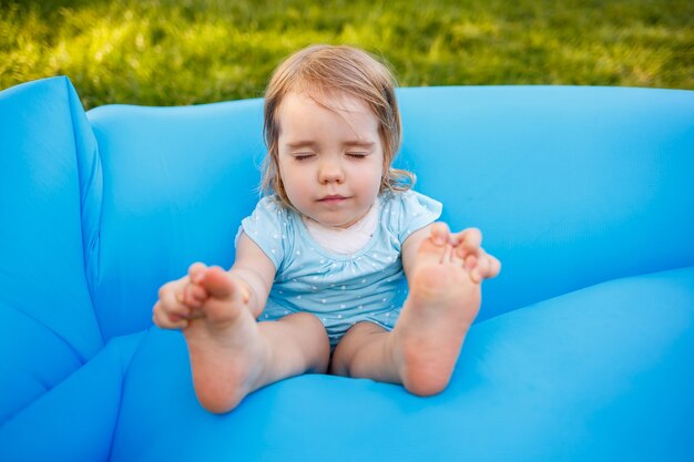 uma menina está descansando e brincando ao ar livre. brincando em um colchão inflável azul