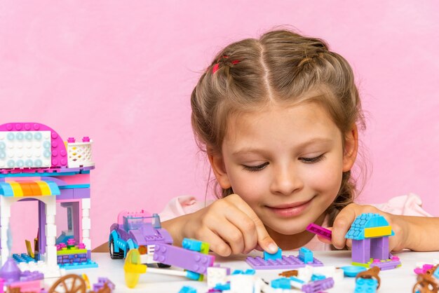 Uma menina está jogando um kit de construção em uma mesa-de-rosa.