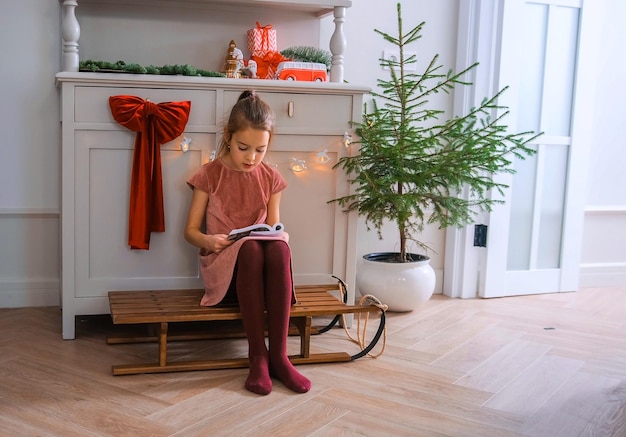 Foto uma menina está lendo um livro em uma sala sentada em um trenó o conceito de ano novo natal férias férias inverno infância