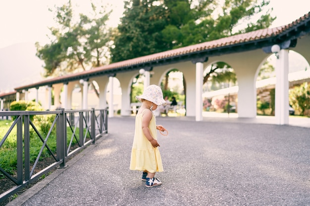 Uma menina está parada no caminho de cascalho perto do pavilhão no parque com um brinquedo nas mãos