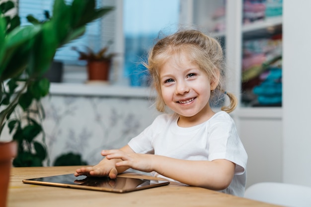 Uma menina está sentada a uma mesa com um tablet com as mãos levantadas no ar sorrindo e feliz